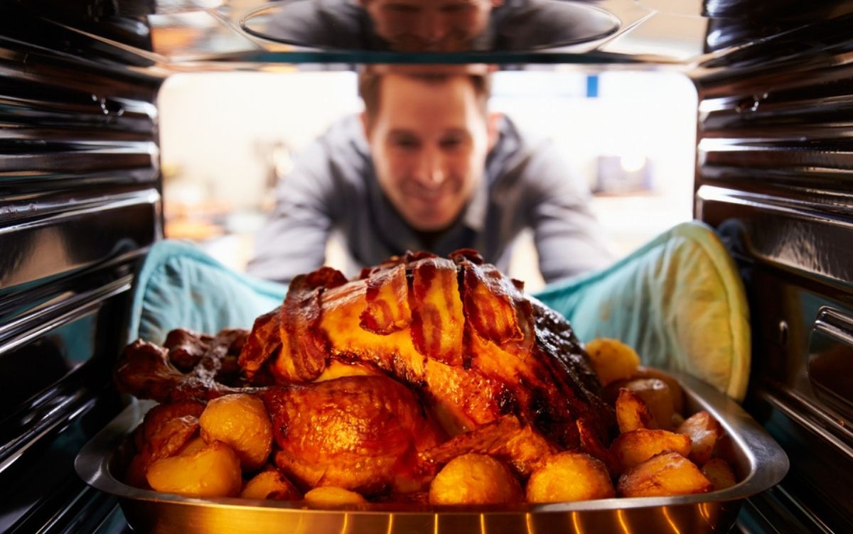 Person smiling as they take a roasted turkey out of the oven, viewed from inside the oven.
