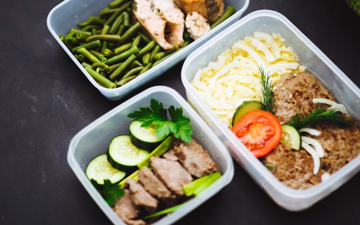 Four meal prep containers with various healthy foods: one with green beans and sliced meat, another with mashed potatoes and meat topped with herbs, one featuring meat slices and cucumber, and the last containing a mixed vegetable and meat dish.