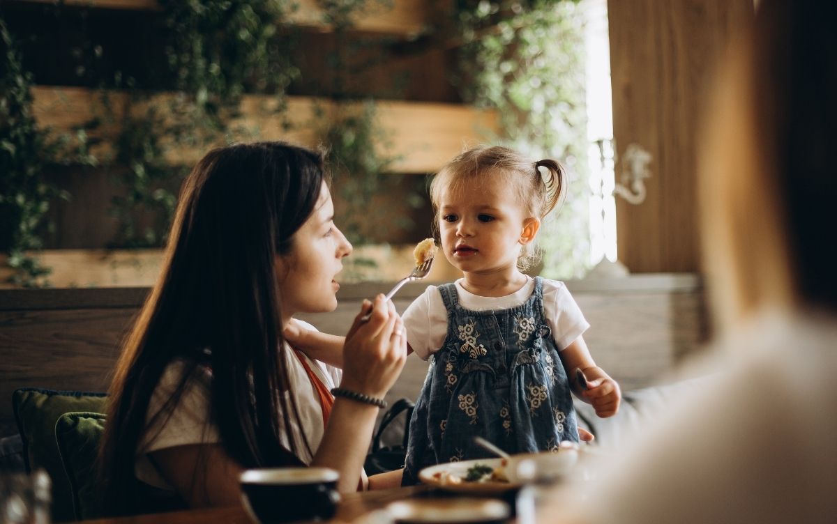 An adult feeding a young child at a table in a cozy dining setting.