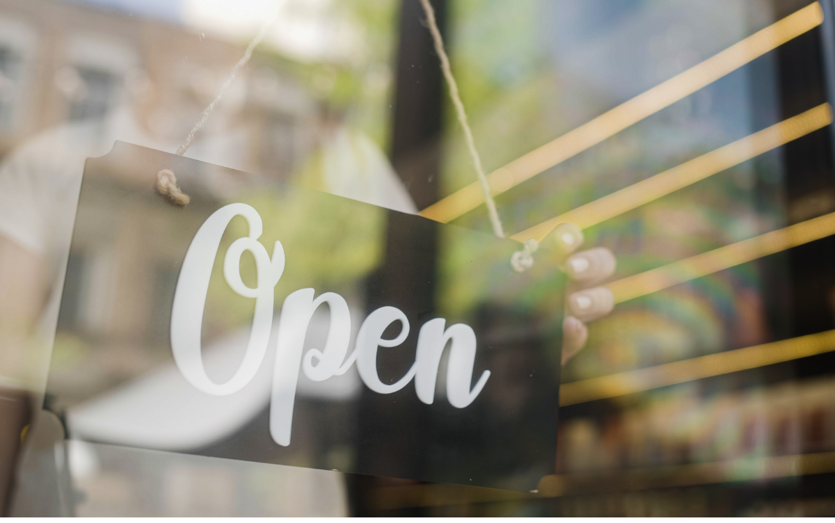 Sign in a restaurant or cafe window being flipped to say it is open by a hand of a member of staff