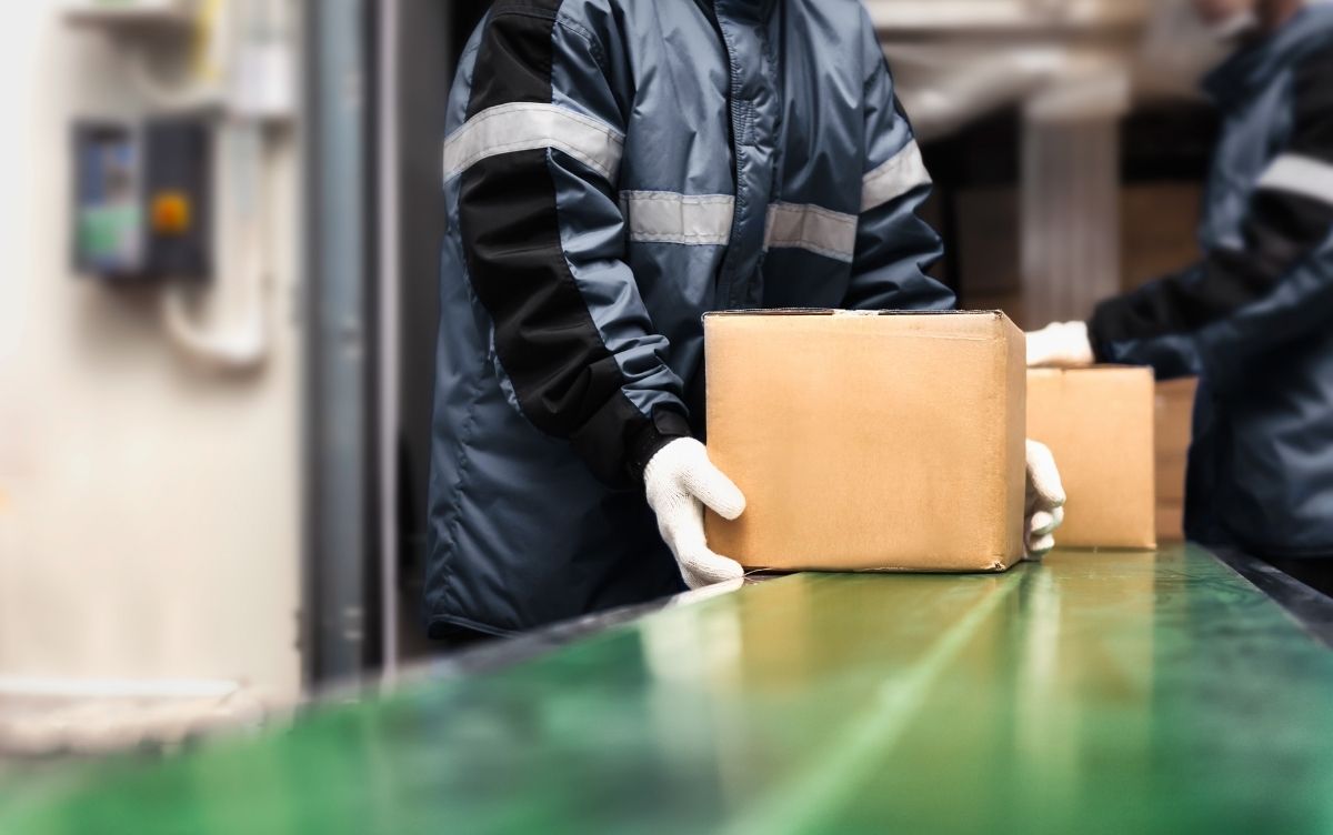 Workers in reflective jackets handling parcels on a conveyor belt in a warehouse.
