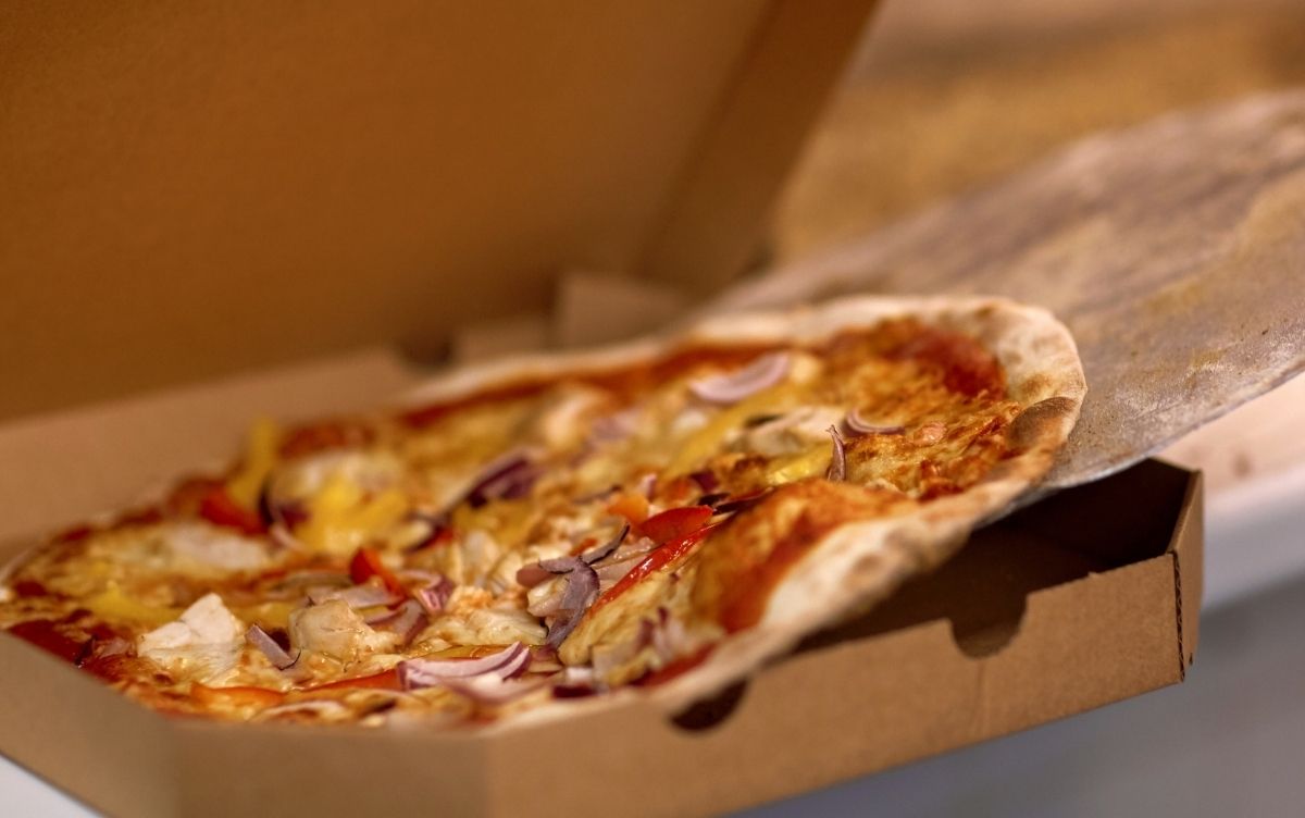A pizza with melted cheese, onion, and other toppings in an open cardboard box.