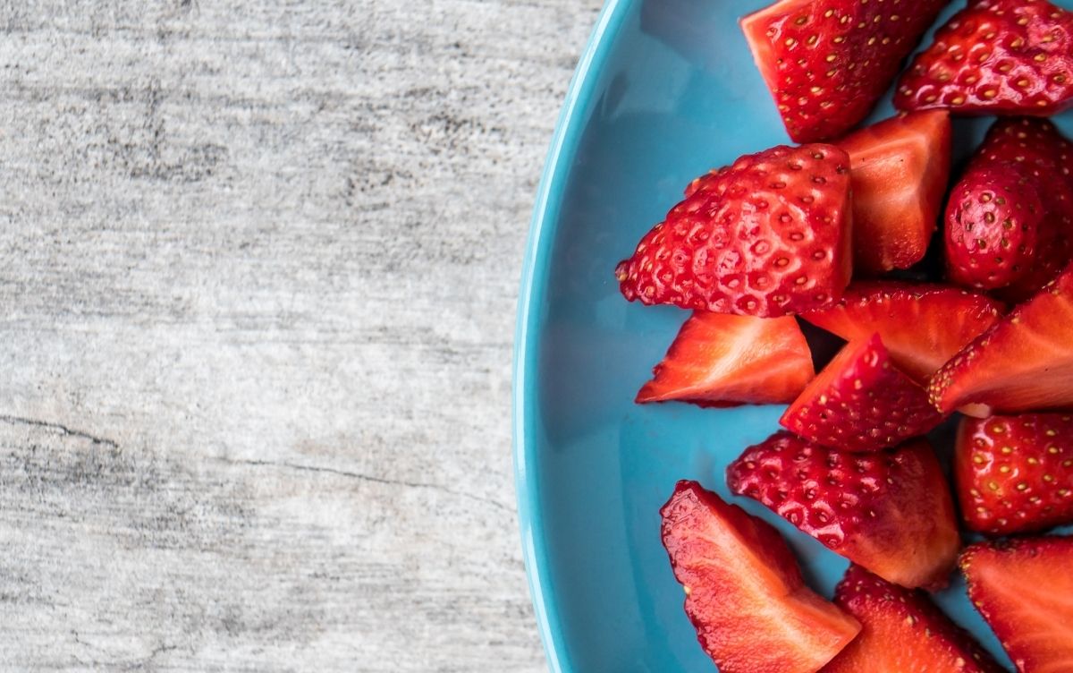 A light blue plate with sliced strawberries arranged on a textured wooden surface.