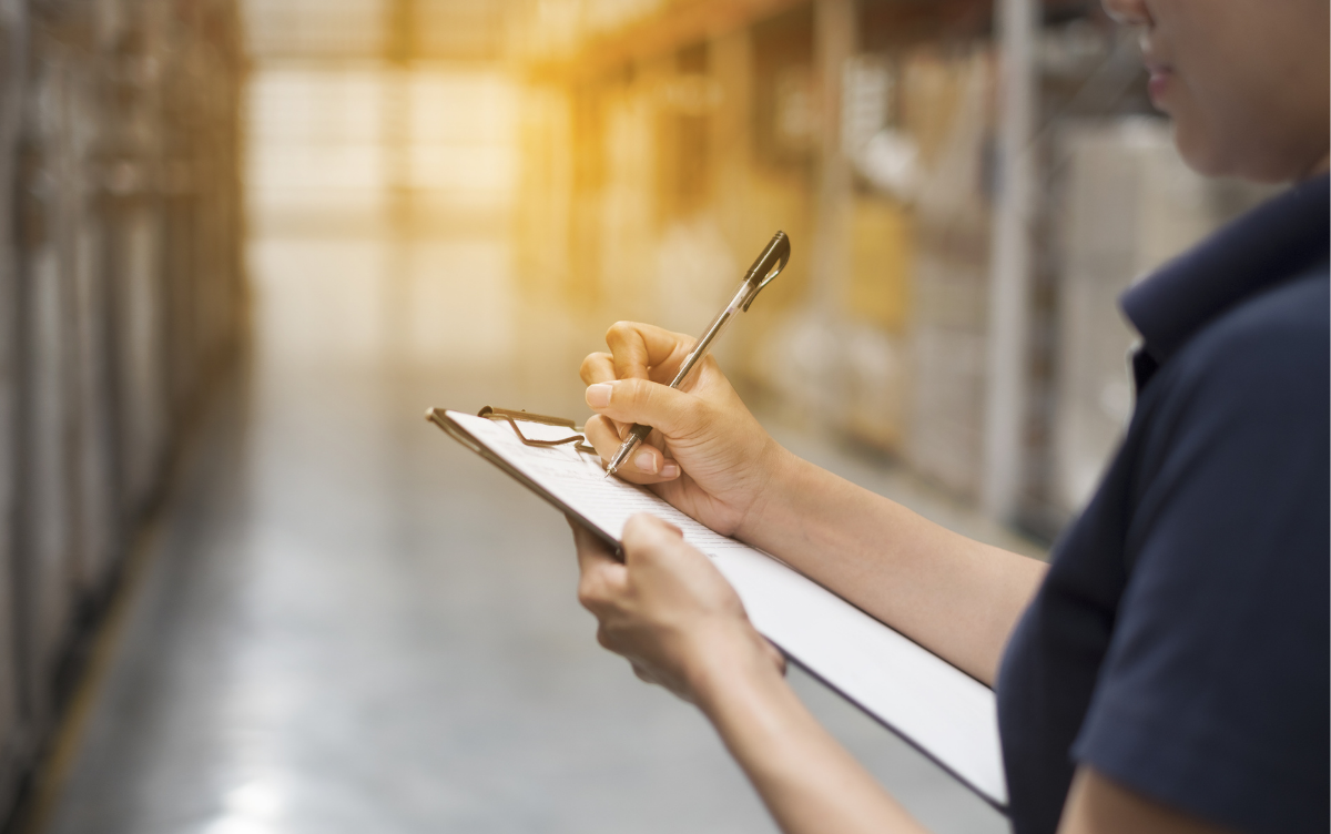 A female hand writes something on a clip board in a standard warehouse