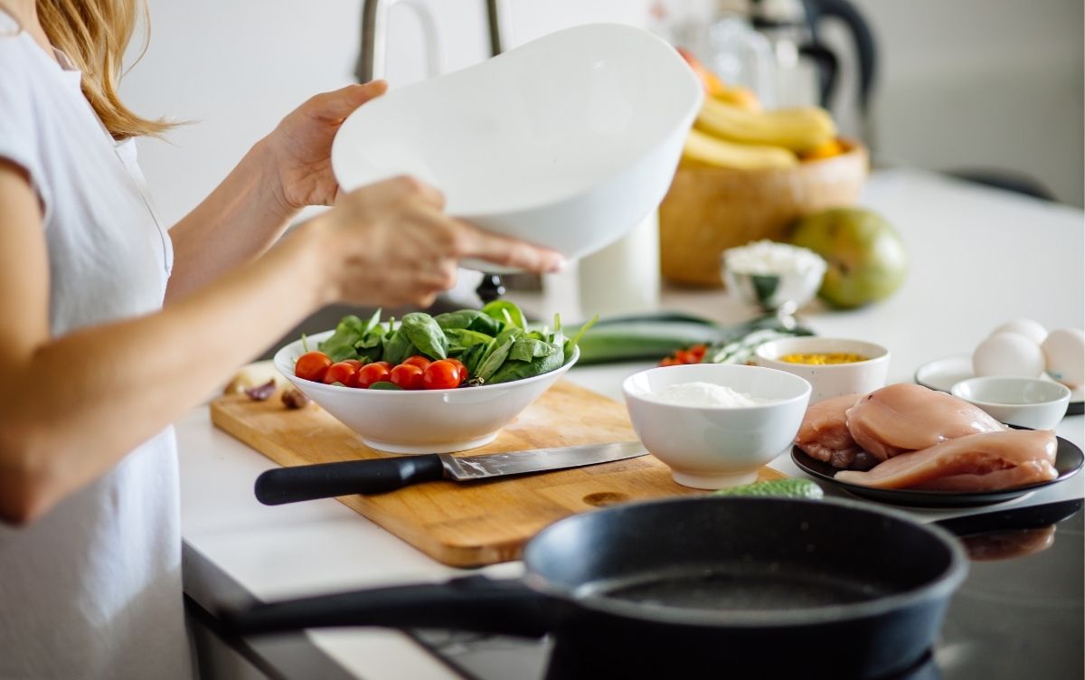 Raw chicken, salad and eggs in separate containers. A woman is preparing to cook using a frying pan.