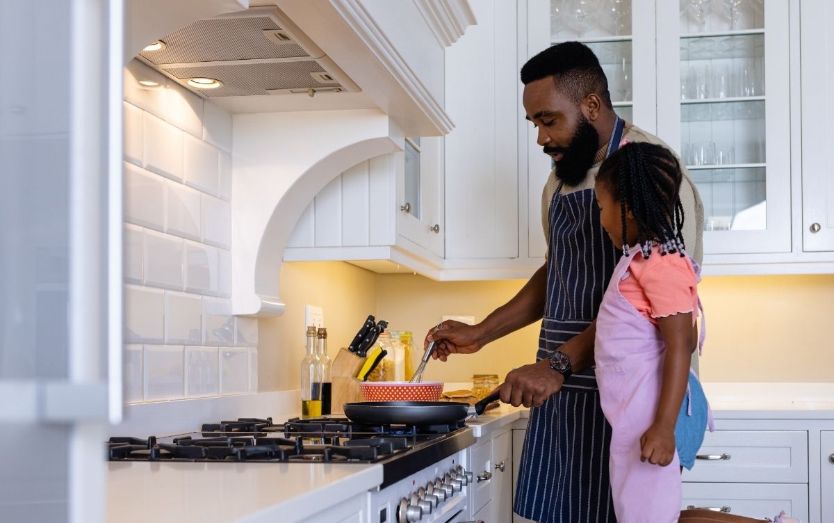 Dad and daughter standing in their kitchen. They're cooking.