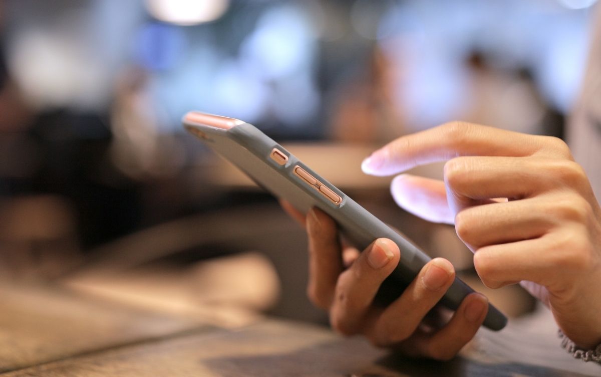 Close-up of a person's hands using a smartphone, with one hand holding the device and the index finger interacting with the screen; blurred background