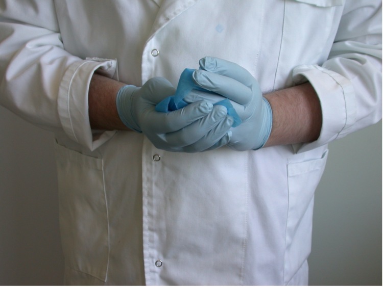 Person wearing a white lab coat and disposable gloves
