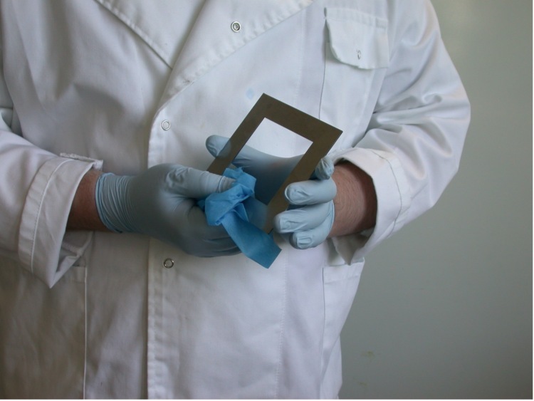 A person cleaning a metal template, wearing gloves and a white lab coat.