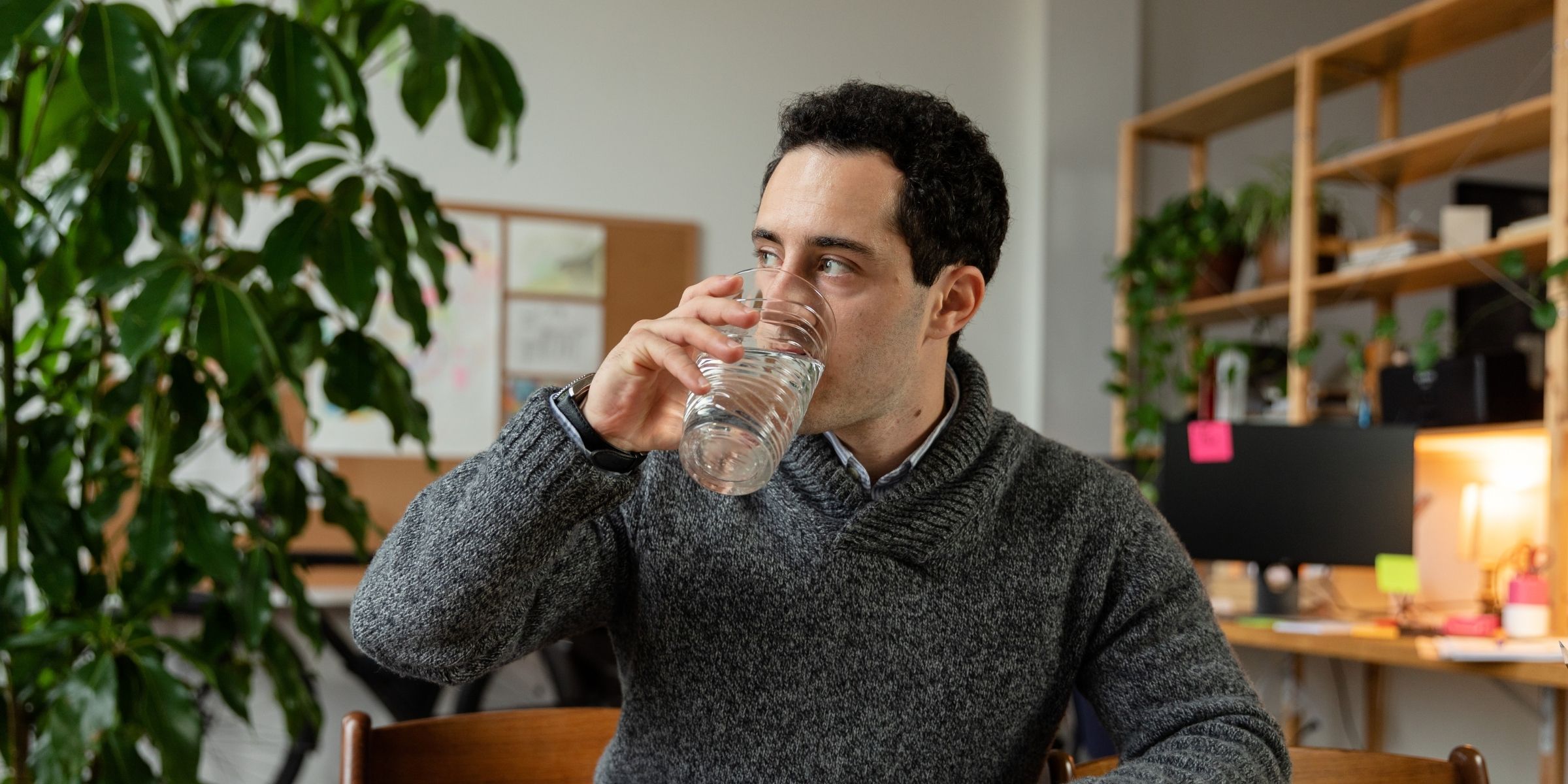 A man sat at a table drinking a glass of water