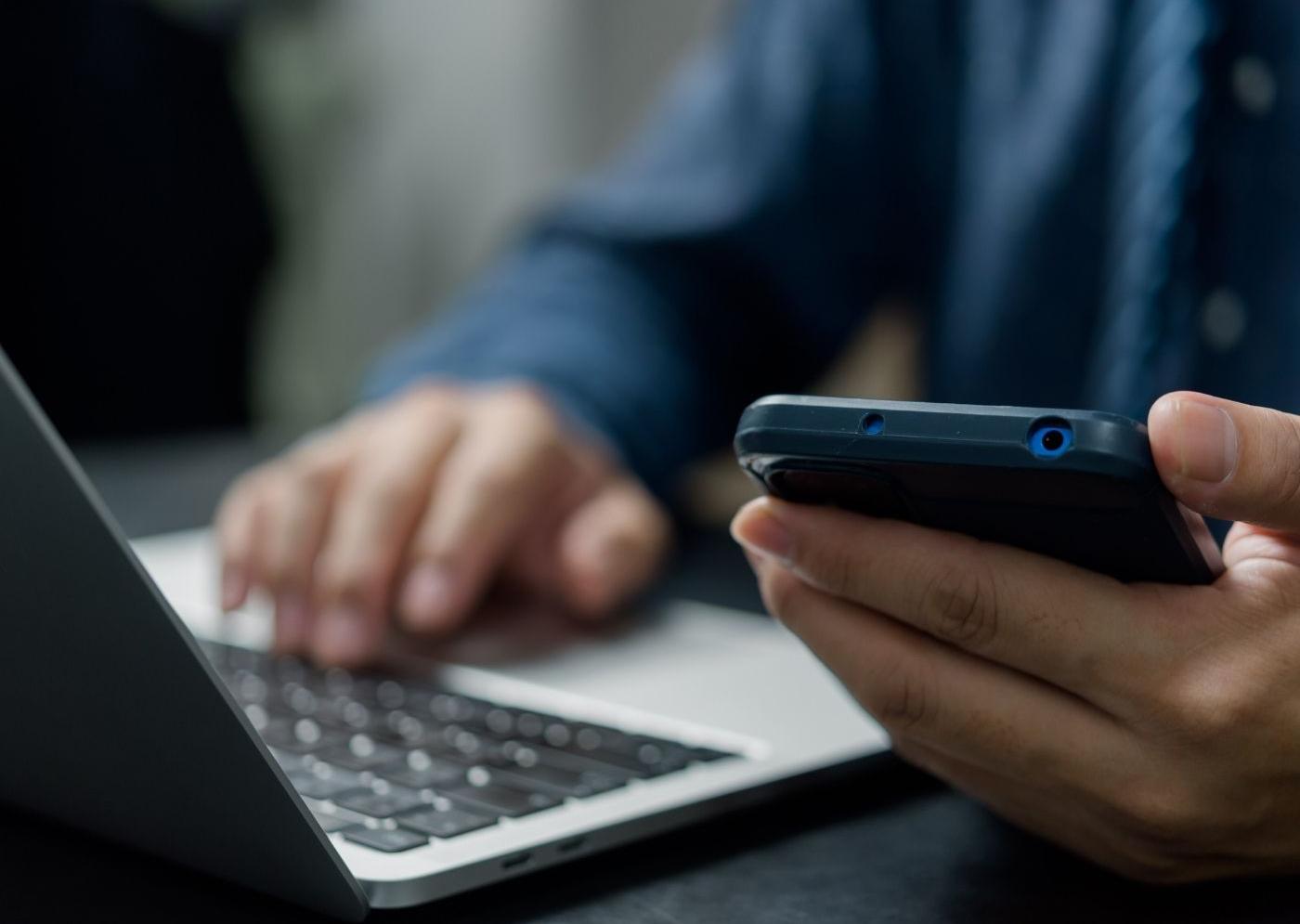 Close-up of a man using a laptop trackpad while holding a smartphone